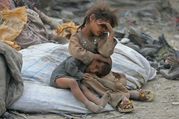 afghan girl holds her brother as they take a break from searching for items to recycle in kabul